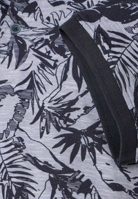 Koszula z krótkim rękawem w szarym materiale z czarnym wzorem liści, z czarnym kołnierzykiem i detalem guzikowym. Teksturowany, pleciony wygląd.