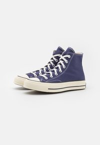 Høj-top sneakers lavet af blå kanvas, med hvide snørebånd, en gummitåhætte og en crèmefarvet sål med sorte striber.