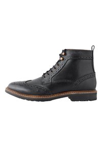 Schwarzer Leder-Stiefelette mit Brogue-Details, Schnürsenkeln mit Metalldringen und einer strukturierten Sohle mit kontrastierendem braunem Rand.