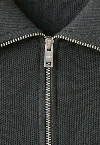 Veste noire en tricot à fermeture éclair avec une fermeture éclair en métal argenté et un col montant, conçue avec un tissu texturé pour plus de chaleur.