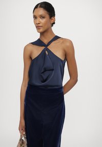 Námořnická modrá saténová halter top s uzlovým detailem na výstřihu, doplněná o odpovídající stmívanou sametovou sukni.