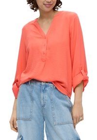 Korallfarbendes, strukturiertes Langarmhemd mit V-Ausschnitt und Knopfleiste, kombiniert mit hellblauen, weit geschnittenen Jeans-Shorts mit Seitentaschen.