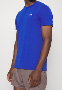 Blå atletisk t-shirt med ett texturerat rutmönster, korta ärmar, rundad halsringning och en liten vit logotyp på bröstet.