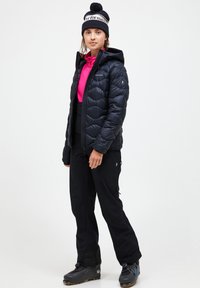 Black puffer jacket with stitched pattern, pink long-sleeve top, black pants, and dark boots. A beanie with a pom-pom completes the outfit.