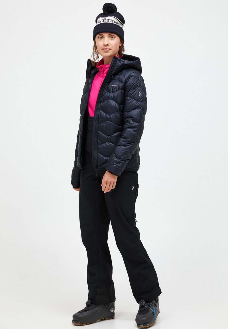 Black puffer jacket with stitched pattern, pink long-sleeve top, black pants, and dark boots. A beanie with a pom-pom completes the outfit.