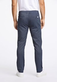 Navy blue chinos made of cotton blend, featuring a straight-leg cut, two back pockets, and belt loops, paired with white sneakers.