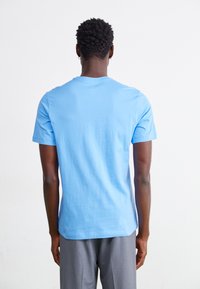 T-shirt de algodão azul com mangas curtas e gola redonda, apresentando uma textura suave e um corte reto na bainha, vista por trás.