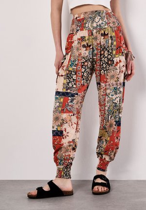 Pantaloni jogger colorati e fantasiosi con disegni floreali, vita elastica e polsini aderenti. Abbinati a sandali neri con suola di sughero.