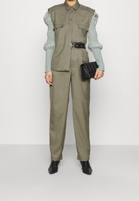 Khaki koszula z zapięciem na guziki i podwójnymi kieszeniami na piersiach, połączona z teksturowanymi rękawami w mięcie. Spodnie z wysokim stanem i czarna kopertówka.