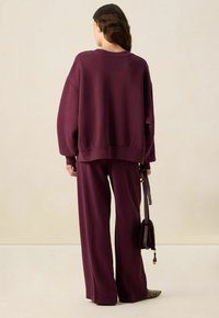 Sweatshirt bordeaux et pantalon large assorti en tissu doux. Coupe ample avec épaules déchues, surface texturée et design minimaliste.