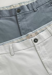 Dos pares de pantalones ajustados, uno gris y otro blanco. Ambos tienen cierres de botón y una cinturilla con patrón y un acento tejido.