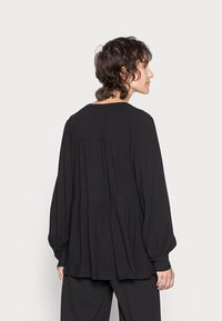 Blusa preta de manga longa com decote redondo, detalhes franzidos na parte de trás e uma silhueta fluida. Feita de um tecido macio e leve.