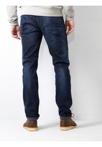 Jeans de mezclilla oscura con corte ajustado, que presentan pierna recta, un desgaste sutil y dos bolsillos traseros. Complementan botas de tobillo casuales marrones.