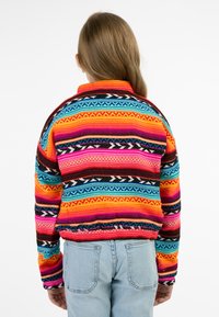 Mehrfarbiger Pullover mit horizontalen Streifen in Pink, Orange, Blau und Schwarz, mit strukturiertem Strick und einem hohen Kragen. 