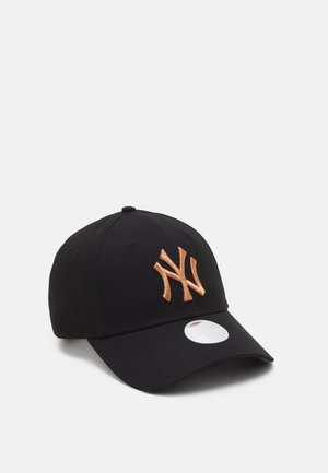 Casquette noire avec une visière incurvée, arborant un logo "NY" brodé en cuivre métallique sur le devant et un autocollant de taille blanc sur la visière.