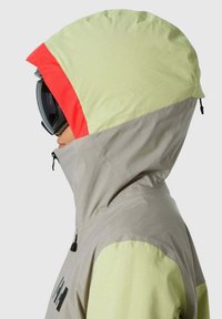 Skijacke mit einem zweifarbigen Design: heller grauer Körper, limonengrüne Ärmelfarben und eine rote Kapuze. Verfügt über einen Reißverschluss und eine verstellbare Kapuze.