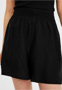 Un short noir avec une taille smockée, fabriqué en tissu léger, avec une coupe ample et sans motifs ni accessoires visibles.