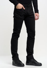 Jeans in denim nero con una vestibilità slim, caratterizzati da un design a cinque tasche e passanti per cintura, abbinati a sneakers alte nere.