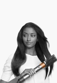 Strumento per acconciare i capelli con una finitura argento e arancione, forma cilindrica, testina con setole, e pulsanti di controllo, tenuto in mano.