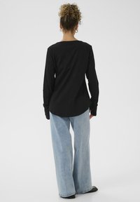 Zwarte long-sleeve shirt met ronde zoom, gecombineerd met lichtblauwe wijde jeans. Glad materiaal met een rechte snit, minimalistisch ontwerp.