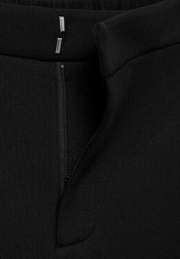 Tessuto nero elasticizzato con una superficie liscia, dotato di una cerniera laterale e due dettagli metallici in vita.
