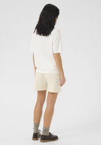 Kortärmad vit topp kombinerad med ljusbeiga shorts, bärs med grå strumpor och mörkbruna skor, vilket visar en avslappnad stil.