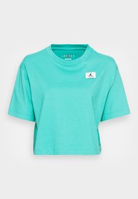 Camiseta recortada de color turquesa, hecha de algodón, con cuello redondo y mangas cortas. Presenta un pequeño parche de logo blanco en la parte delantera.