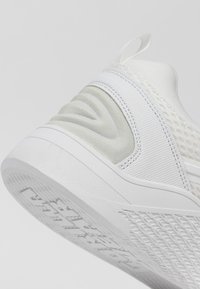 Witte sneaker met een gestructureerde, mesh bovenkant, een gladde rubberen tussenzool en een geprofileerde rubberen buitenzool. Subtiele accenten in een lichte tint.
