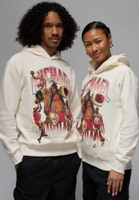 Kermansävyisissä huppareissa on värikäs Michael Jordan -kuva koripalloteemoilla, teksturoitua kangasta ja kengurupussit, joita käyttävät kaksi mallia.