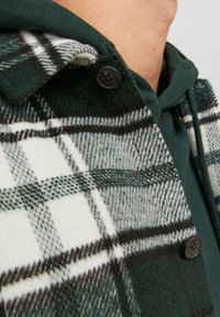 Wollhemdjacke in grün-weißer Karomusterung mit schwarzen Akzenten. Verfügt über einen Klappkragen, einen Knopfverschluss und eine weiche Textur.