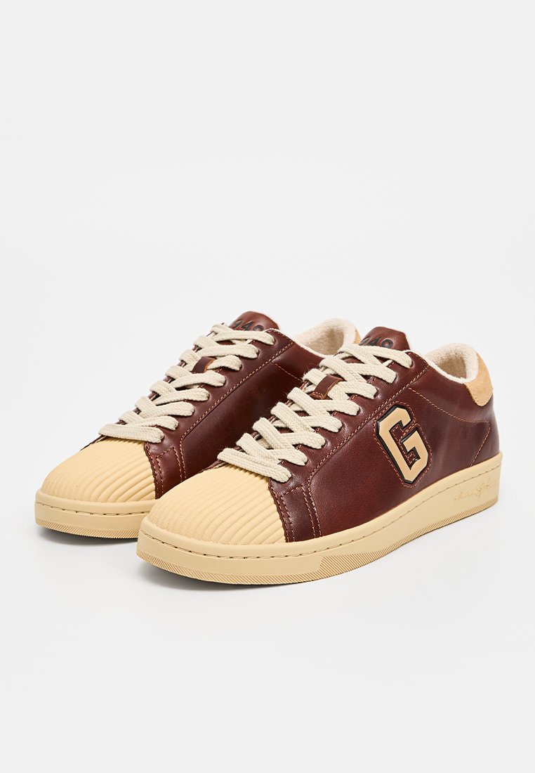 Brązowe skórzane sneakersy z beżowym gumowym noskiem w rybkę, beżowymi sznurówkami i dużym logo "G" po boku. Miękka podszewka dla komfortu.