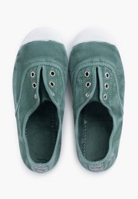 Zapatillas de lona verde sin cordones, con puntera de goma blanca, ojales de metal y forro interior texturizado. Presenta un diseño simple y minimalista.