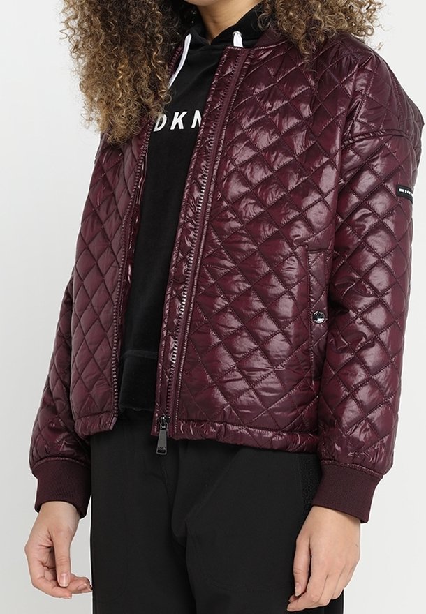 Bordeaux geklede bomberjack met glanzende afwerking, geribbelde manchetten en ritssluiting. Bevat zijzakken en heeft een getailleerd ontwerp.