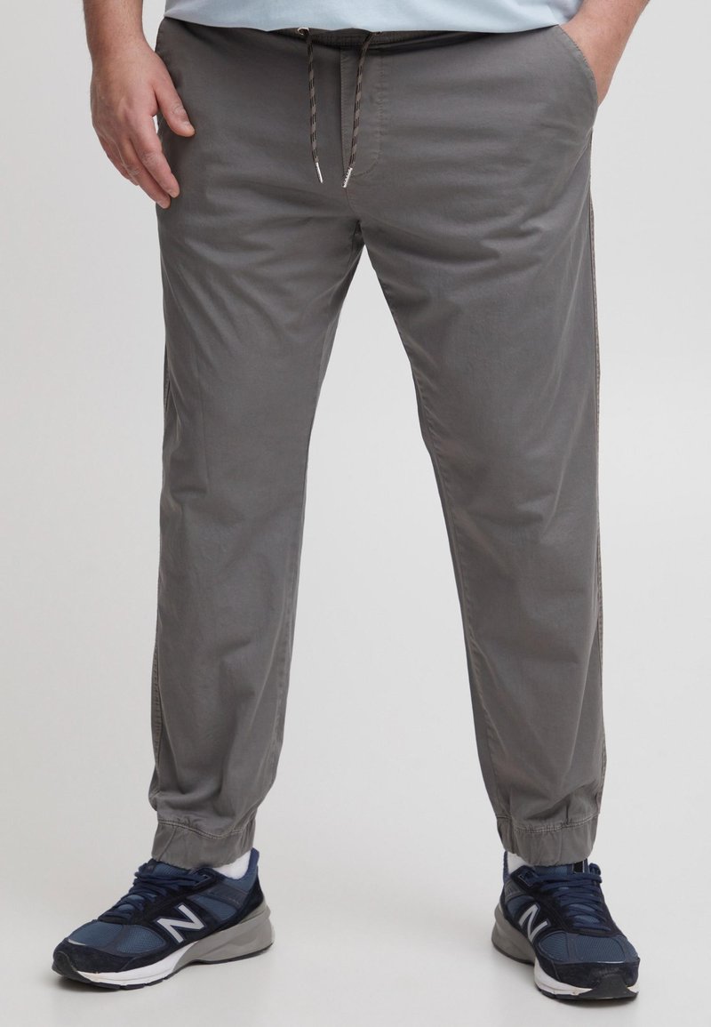 Pantaloni jogging gri deschis, cu talie elastică și șnur ajustabil, având buzunare laterale și manșete elastice la glezne.