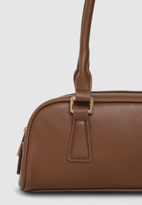 Braune Handtasche aus Kunstleder mit strukturierter Form, ausgestattet mit einem oberen Griff und goldfarbenen Beschlägen. Glatte Textur mit sichtbaren Nähten.