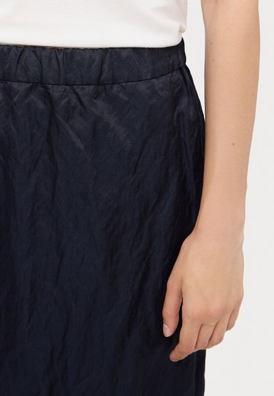 Dark navy skirt featuring a textured, crinkled fabric with an elastic waistband. The hand shows a smooth, light skin tone.
