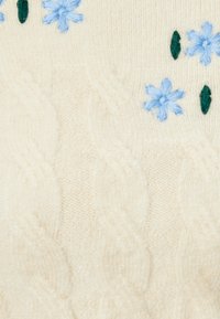 Krämfärgad kabelstickad tröja med blå broderade blommor och gröna blad. Mjuk textur med upphöjda mönster och blommiga detaljer.