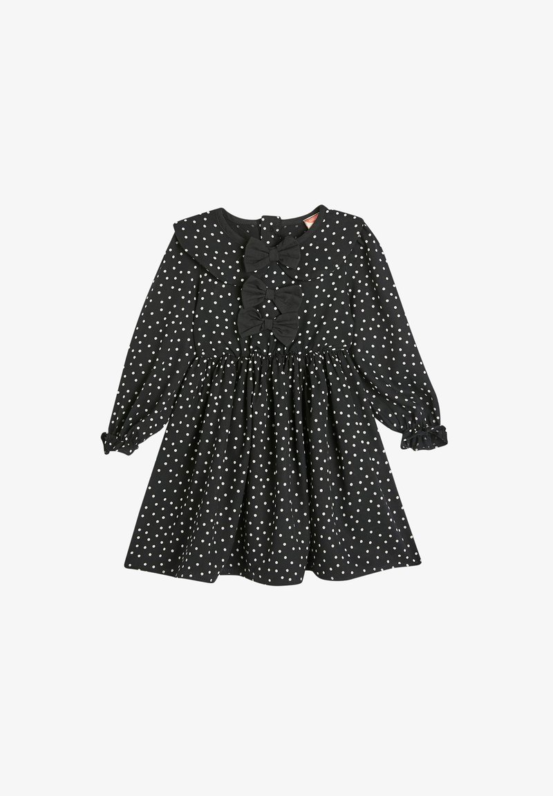 Svart klänning med prickar, långa ärmar, volangkrage, tre tygrosetter framtill och elastiska ärmar. Tillverkad av mjukt material.