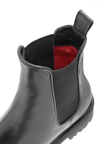 Czarne skórzane botki Chelsea z elastycznymi bocznymi panelami, teksturowaną powierzchnią i czerwoną podszewką, z niskim obcasem i trwałą podeszwą.