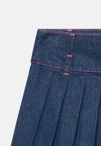 La gonna di jeans presenta un design plissée con un colore blu scuro e una leggera lucentezza. Sono presenti dettagli di cucitura rossa vicino alla vita.