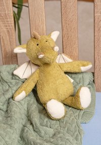 Soft yellow dragon plush toy with white wings and feet sits on a green knitted blanket draped over a wooden chair.