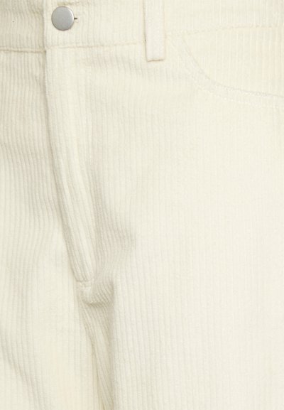 Calças de tecido de corduroy branco com fecho de correr, design de cinco bolsos e um botão de metal prateado. A superfície texturizada oferece um interesse visual.