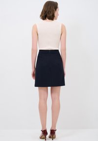 Ärmelloses, cremfarbenes Top kombiniert mit einem dunkelblauen Minirock, der eine glatte Textur, ein tailliertes Design und einen Reißverschluss auf der Rückseite aufweist.