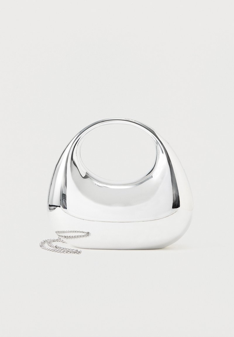 Λαμπερή, ασημί μεταλλική τσάντα χειρός με στρογγυλεμένο σχήμα, οβάλ λαβή κομμένη στο κέντρο και ασημένιο λουρί αλυσίδα σε μονόχρωμο ανοιχτό φόντο.