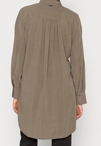 Chemise à manches longues couleur khaki avec col, détail de dos plissé, poignets à boutons et ourlet arrondi, en tissu léger.