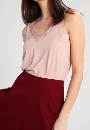 Lyserød ærmeløs top med blonder langs halsudskæringen, kombineret med et højtaljet bordeauxnederdel. Blødt stof og skræddersyet pasform.