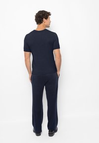 Donkerblauw overhemd met korte mouwen en ronde hals, gecombineerd met bijpassende losse broek met twee achterzakken, van achteraf weergegeven.