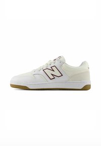 Zapatilla blanca de corte bajo con suela de goma, logo "N" color granate en el lateral, cordones blancos y panel trasero de ante.