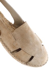 Beiger Wildlederschuh zum Hineinschlüpfen mit Ausschnitten und gewebter Jutesohle. Glatte Textur und runder Zehenbereich mit handgenähten Akzenten.