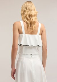Top bianco senza maniche con orlo arricciato, caratterizzato da rifiniture nere. Texture liscia e design aderente con chiusura a zip sul retro.
